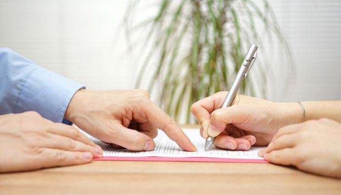 man pointing where the woman should place the sign in the agreement